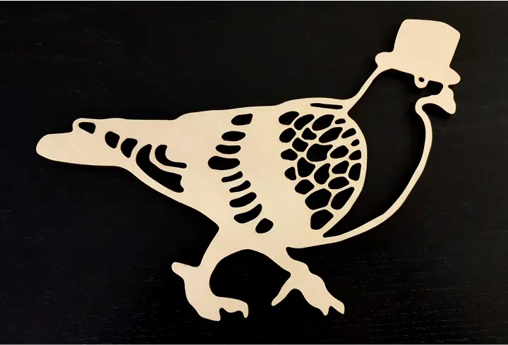 A laser cut wooden pigeon decoration featuring intricate feather patterns and wearing a top hat. The design is cut from light-colored plywood and photographed against a black background, showing detailed cutouts that create the bird's distinctive shape and texture.